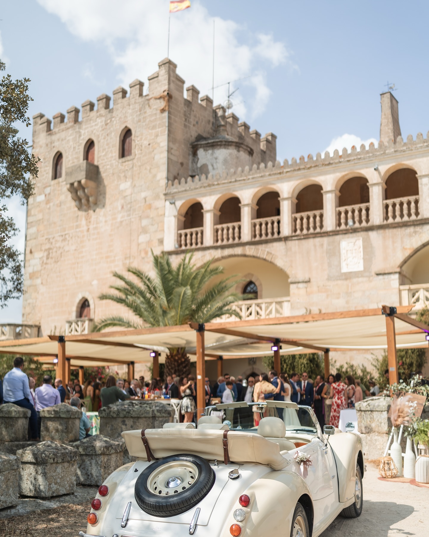 Recepción de invitados en un castillo con coche clásico blanco descapotable y decoración para evento elegante.
