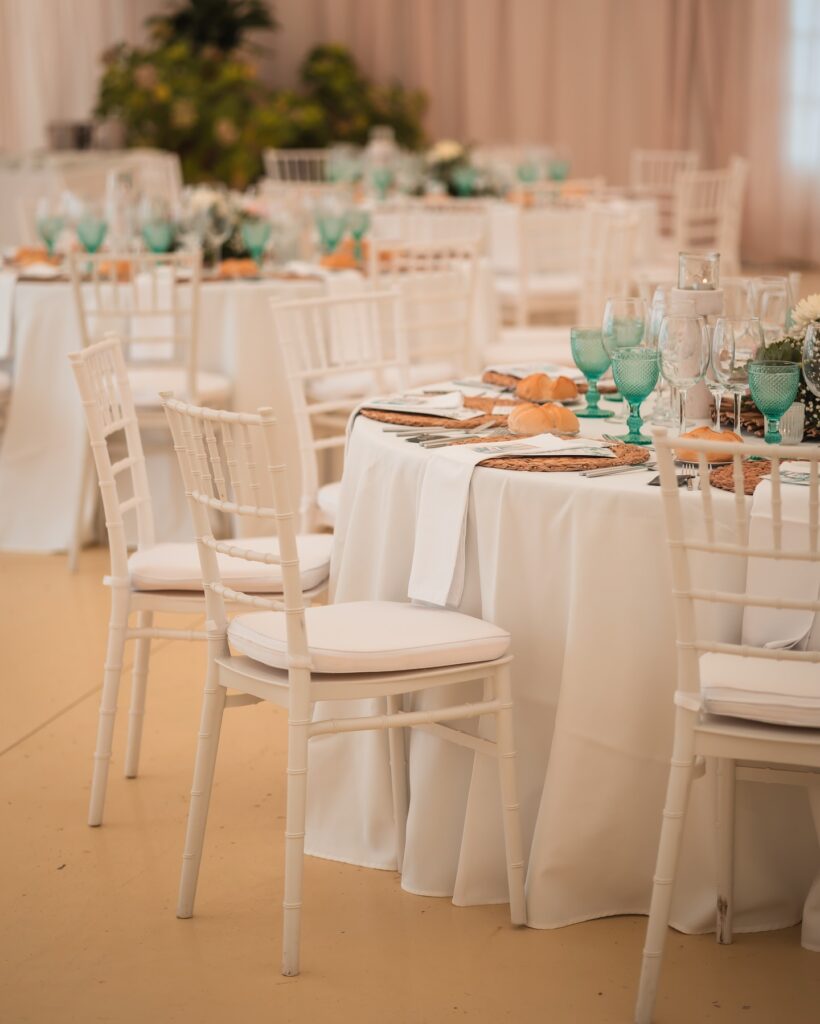 Mesa redonda elegantemente decorada con mantelería blanca y copas verdes en salón de celebraciones, lista para evento.